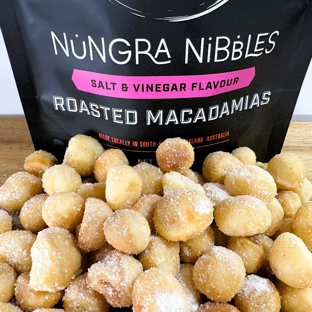 A bag of Nungra Nibbles Salt & Vinegar Roasted Macadamias with a pile of macadamia nuts covered in seasoning in front of it.
